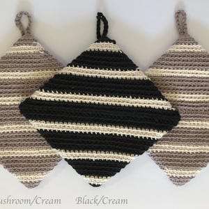 Op de afbeelding: Drie gehaakte ovenwanten met gestreepte patronen. De ovenwanten zijn in de kleuren champignon/room, zwart/room en room/champignon.