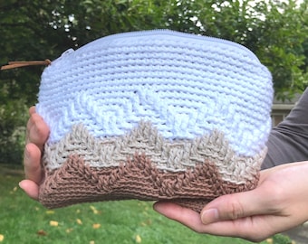 Peut inclure: Une pochette crochetée avec une fermeture éclair. La pochette présente un dégradé de couleurs, passant du blanc au bleu clair, puis au beige et au marron à la base. Une petite tirette en cuir est attachée à la fermeture éclair.