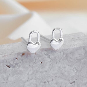 Puede incluir: Un par de pendientes de botón de plata en forma de corazón con cierre. Los pendientes son pequeños y delicados, y serían un gran regalo para alguien especial.