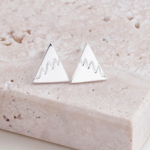 Könnte beinhalten: Ein Paar silberne Dreiecksohrringe mit einem Bergketten-Design.