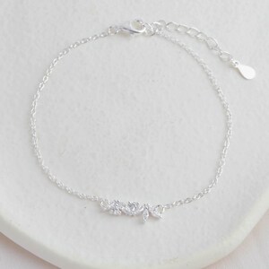 May include: A delicate silver chain bracelet with a small cluster of clear cubic zirconia stones in the shape of leaves.