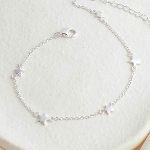 May include: A silver bracelet with star-shaped charms. The bracelet has a chain design with an adjustable length and a clasp. The stars are evenly spaced along the chain, creating a celestial theme. The bracelet is made of silver.