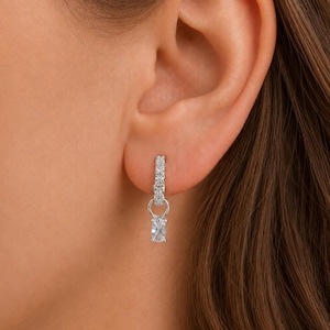 May include: A silver-toned hoop earring featuring a row of small, clear, sparkling stones along the band. A single, vertically oriented, rectangular-cut clear stone hangs from the bottom of the hoop, secured by a small circular metal link.