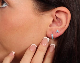May include: A close-up of a person's hand wearing a silver ring with a turquoise flower design. The person is also wearing a pair of small turquoise hoop earrings and a single turquoise stud earring.