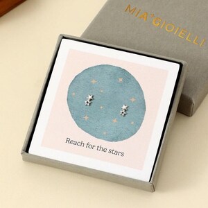 Könnte beinhalten: Sternförmige Ohrstecker in einer grauen Schachtel mit dem Text "MIA GIOIELLI". Die Ohrringe werden auf einer Karte mit einem tealfarbenen Kreis und den Worten "Reach for the stars" präsentiert.