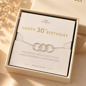 Op de afbeelding: Een ketting van sterling zilver met drie in elkaar grijpende ringen in een crèmekleurige geschenkdoos. De presentatiekaart bevat de tekst HAPPY 30TH BIRTHDAY en THIS SPECIAL PIECE IS JUST TO SAY HAVE A WONDERFUL 30TH BIRTHDAY met MIA GIOIELLI.
