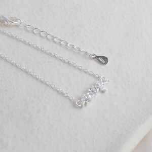 May include: A silver necklace with a delicate chain and a small, sparkling pendant shaped like a cluster of leaves. The pendant is adorned with tiny, clear cubic zirconia stones. The necklace has a lobster clasp closure and a tag with the inscription "AG925".