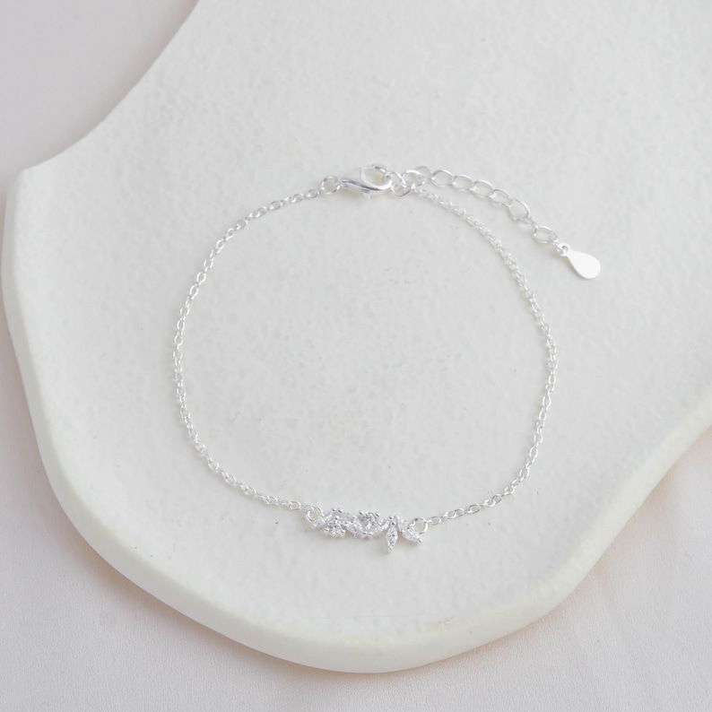 May include: A delicate silver chain bracelet with a small cluster of clear cubic zirconia stones in the shape of leaves.