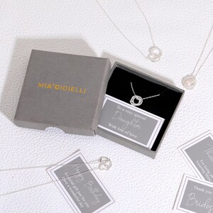 Pu&ograve; includere: Una collana in argento con ciondolo circolare all'interno di una scatola regalo grigia con l'etichetta MIA GIOIELLI. La scatola include un biglietto con la scritta To a very special Daughter With lots of love. Altre collane e biglietti sono visibili.