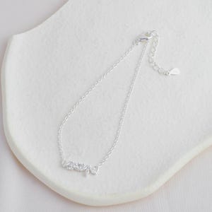 May include: A silver chain bracelet with a delicate, sparkling leaf design. The bracelet has a lobster clasp closure.