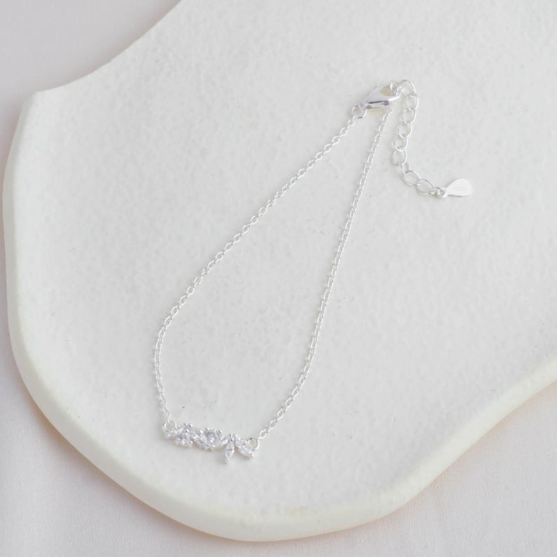 May include: A silver chain bracelet with a delicate, sparkling leaf design. The bracelet has a lobster clasp closure.