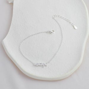 May include: A delicate silver chain bracelet with a small cluster of clear cubic zirconia stones in the shape of leaves.