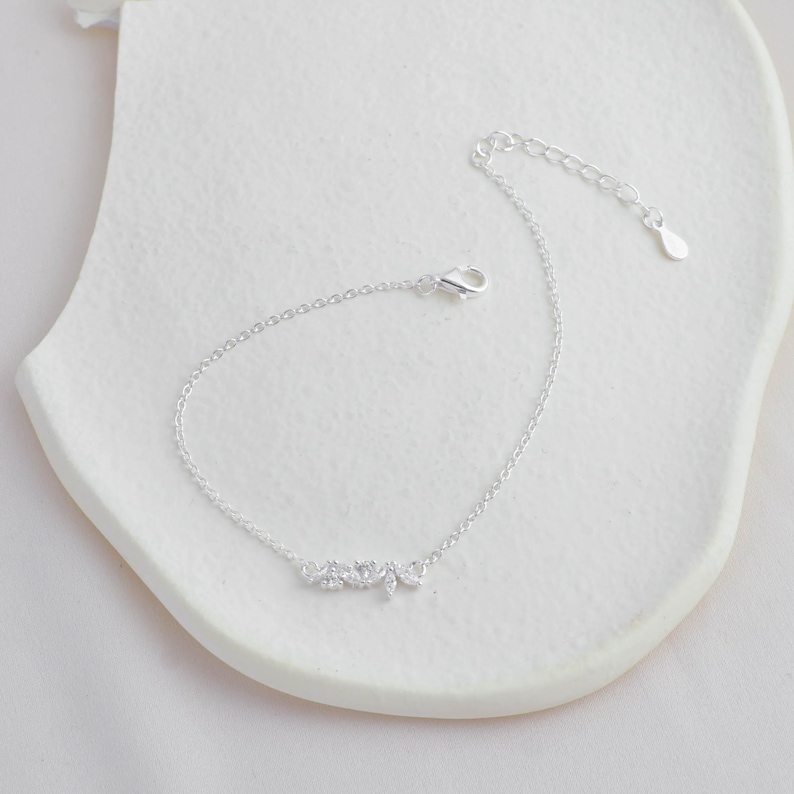 May include: A delicate silver chain bracelet with a small cluster of clear cubic zirconia stones in the shape of leaves.