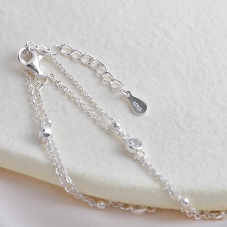 Puede incluir: Un brazalete de cadena de plata con un dise&ntilde;o delicado. El brazalete presenta peque&ntilde;as piedras transparentes y una etiqueta de plata con la inscripci&oacute;n "AG925".