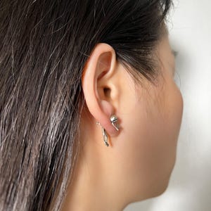 May include: A pair of silver earrings, one featuring a small hand and the other a small sphere.