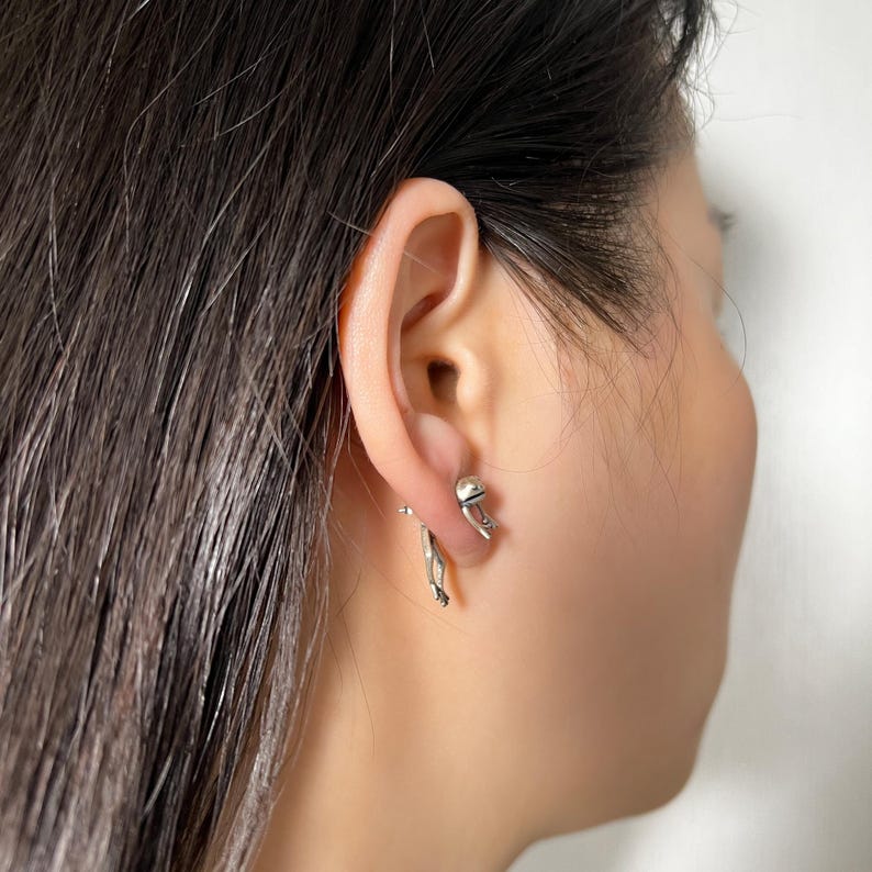 May include: A pair of silver earrings, one featuring a small hand and the other a small sphere.