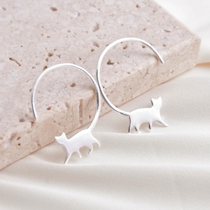May include: A pair of silver hoop earrings featuring a cat silhouette design. The earrings are simple and elegant, ideal for everyday wear.