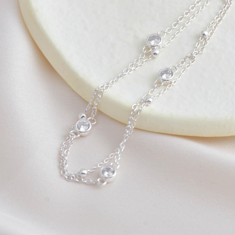 Puede incluir: Un collar de cadena de plata con una doble cadena y peque&ntilde;as piedras transparentes.