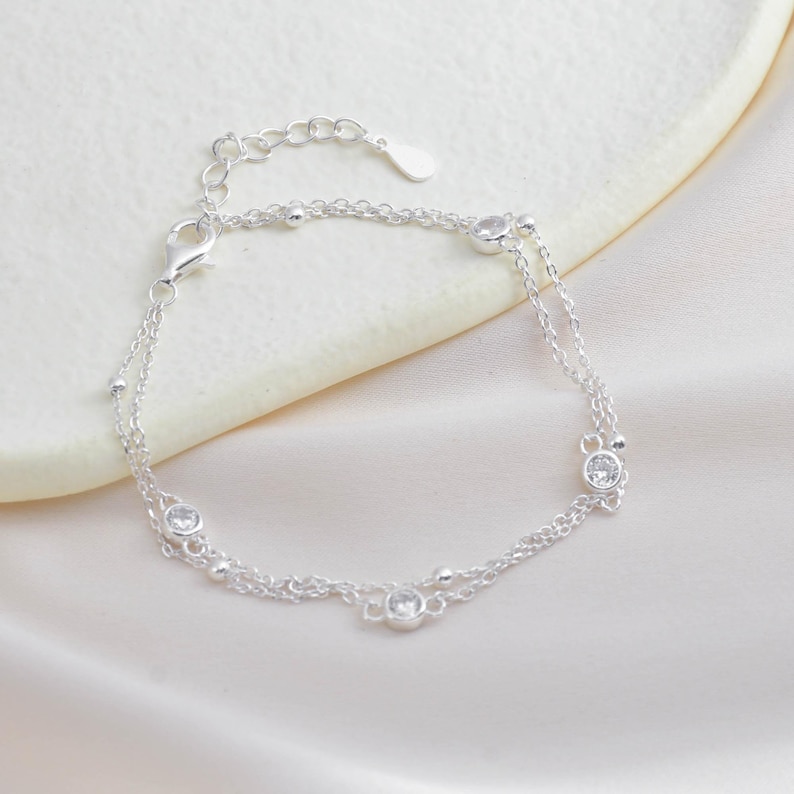 Puede incluir: Un delicado brazalete de cadena de plata con una doble cadena y peque&ntilde;as piedras de circonita c&uacute;bica transparentes.