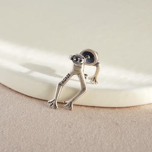 May include: Silver frog earring with a post back. The back of the earring is stamped with the text "AG925".
