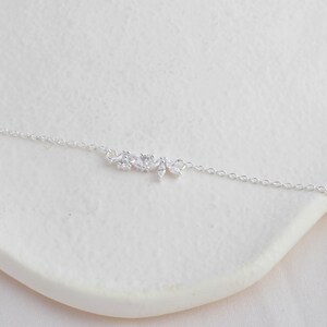 May include: A delicate silver chain necklace with a small, sparkling floral design pendant.