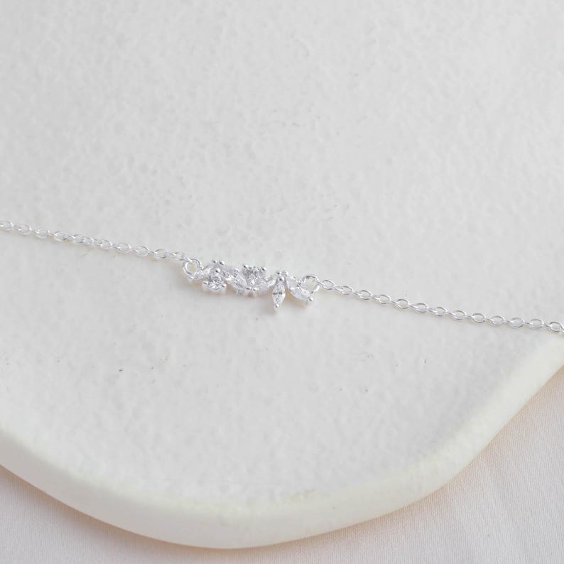 May include: A delicate silver chain necklace with a small, sparkling floral design pendant.