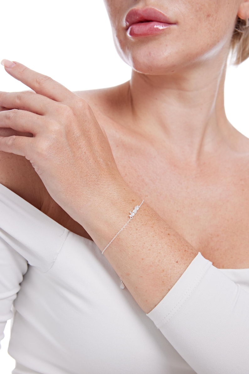 May include: A delicate silver chain bracelet with small, clear cubic zirconia stones. The bracelet is shown on a person's wrist.