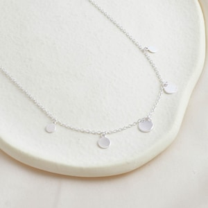 May include: A silver necklace with a delicate chain and four small, round silver charms hanging from it.