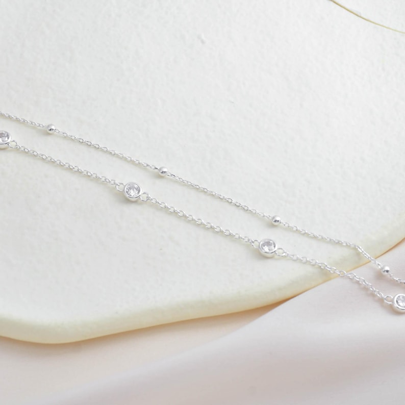 Puede incluir: Un delicado collar de cadena de plata con peque&ntilde;as piedras de circonita c&uacute;bica transparentes. El collar tiene un dise&ntilde;o en capas con dos cadenas.
