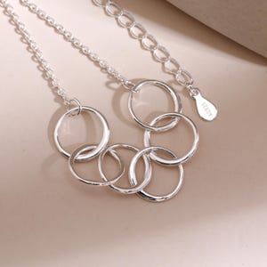 Pu&ograve; includere: Una collana d'argento con un design di cerchi aperti interconnessi. La collana ha una catena sottile e una chiusura regolabile. Il metallo ha una finitura brillante e riflettente. L'etichetta recita "AG925".