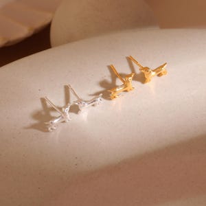 Op de afbeelding: Twee paar teckel oorknopjes, &eacute;&eacute;n zilver en &eacute;&eacute;n goud. De oorbellen zijn miniatuur hondjes met gedetailleerde kenmerken. Gepresenteerd op een lichtgekleurd oppervlak, dat hun ontwerp benadrukt.