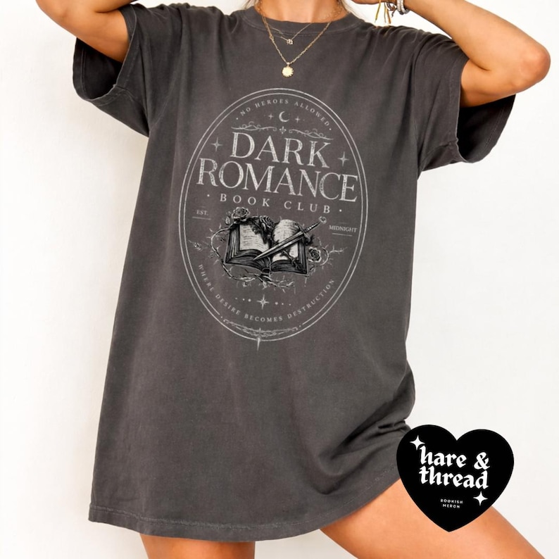 Puede incluir: Camiseta gris oscuro con un dise&ntilde;o circular que dice "Dark Romance Book Club" con un libro abierto y rosas. La camiseta tambi&eacute;n tiene el texto "No Heroes Allowed" y "Where Desire Becomes Destruction".
