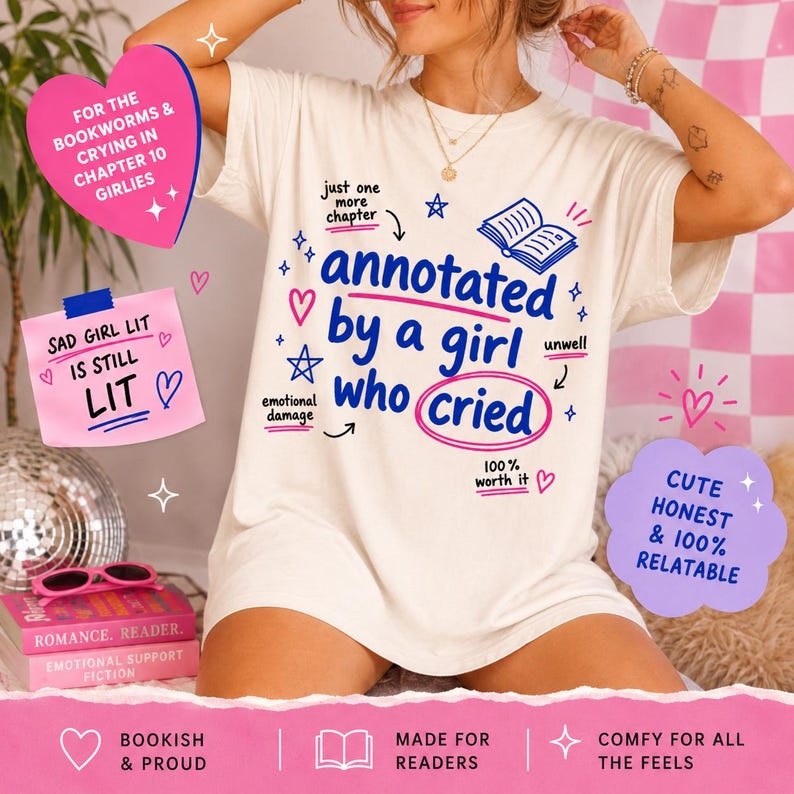 Op de afbeelding: Cr&egrave;mekleurig T-shirt met de tekst "annotated by a girl who cried" in blauw en roze. Het shirt heeft extra tekst en afbeeldingen, waaronder harten, sterren en de woorden "Sad Girl Lit is Still Lit".