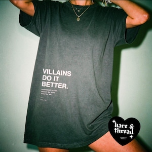 Puede incluir: Camiseta gris oscuro con el texto "VILLAINS DO IT BETTER" en blanco. La camiseta también presenta el texto "understood by few, chosen by none, loved by me." Un logotipo negro en forma de corazón con las palabras "hare & thread" es visible.