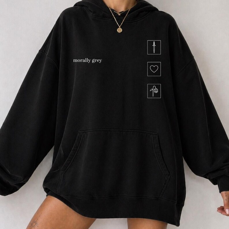 May include: Black hoodie with a front pocket and a drawstring hood. The text "morally grey" is printed on the front. Three white line drawings of a knife, heart, and flower are on the right side of the hoodie.
