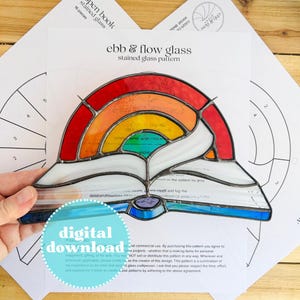 May include: A stained glass rainbow in the shape of an open book, featuring red, orange, yellow, green, and blue hues. The design is held over a printed pattern sheet. The words "ebb & flow glass" and "digital download" are visible.