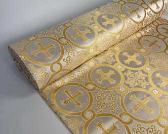Puede incluir: Un rollo de tela con un patrón repetitivo de cruces doradas y motivos de volutas intrincadas sobre un fondo beige claro. El diseño consiste en marcos circulares que contienen cruces, alternando con patrones ornamentales de tipo floral.