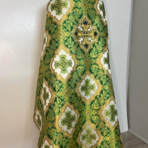 May include: A green and gold liturgical vestment with a cross pattern. The vestment is made of a brocade fabric with a floral design.