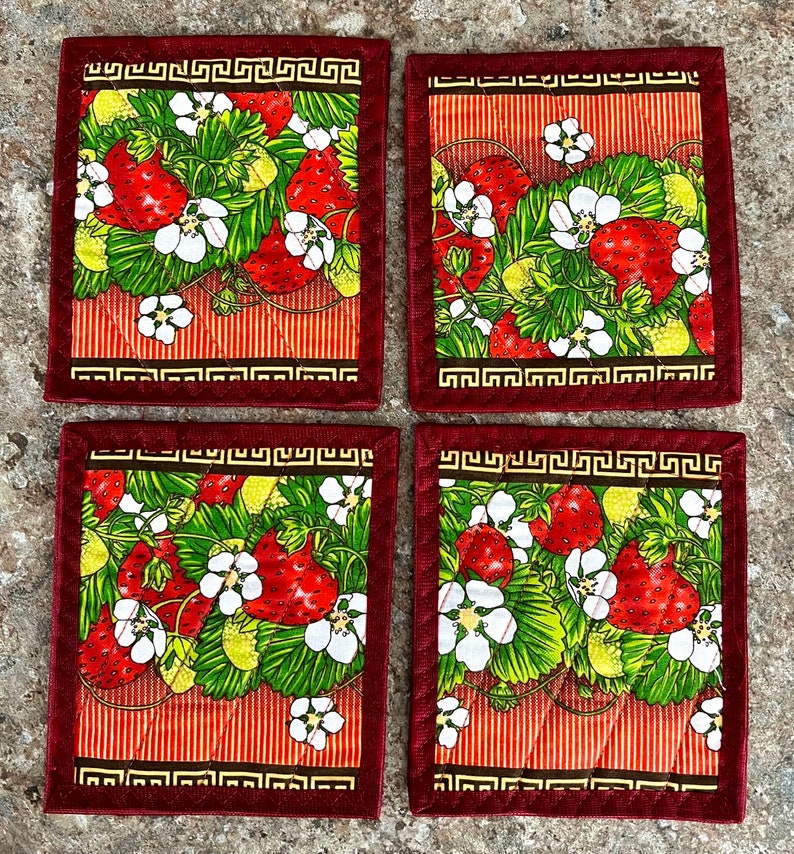 May include: Set of four square coasters featuring a vibrant strawberry design. Each coaster has a red border with a Greek key pattern, surrounding a pattern of red strawberries, green leaves, and white flowers on a striped background.