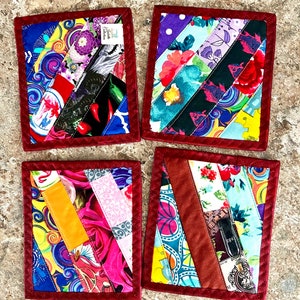 May include: Set of four handmade fabric coasters. Each coaster features a patchwork design with diagonal strips of colorful patterned fabric, including floral, abstract, and geometric prints. The coasters are bordered with a dark red fabric and have a square shape.
