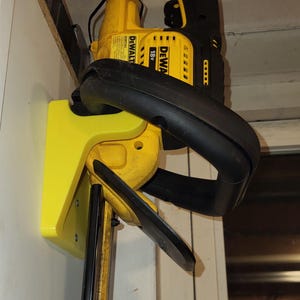 Op de afbeelding: Een gele en zwarte wandbevestiging voor een DeWalt 18v snoerloze heggenschaar. De beugel is gemaakt van plastic en heeft een eenvoudig ontwerp. Hij wordt met schroeven aan een muur bevestigd.