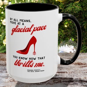 Puede incluir: Taza de cerámica blanca con interior y asa negros. La taza presenta texto rojo y un gráfico de zapato de tacón alto rojo. El texto incluye "BY ALL MEANS, MOVE AT A glacial pace" y "YOU KNOW HOW THAT thrills me."
