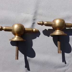 Könnte beinhalten: Zwei goldfarbene Türknauf aus Metall mit einer runden Kugelform und einem Querbalken. Die Knäufe sind an einer Metallstange befestigt.