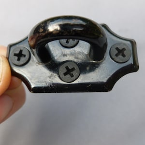 Könnte beinhalten: Schwarzer Metallhaken mit einer abgerundeten Schlaufe und vier Kreuzschlitzschrauben.