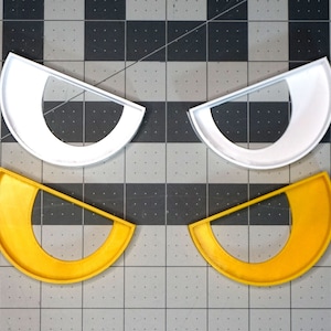 May include: Two pairs of cookie cutters, one white and one yellow. The cutters are shaped like a crescent moon with a smaller crescent moon cut out of the center.