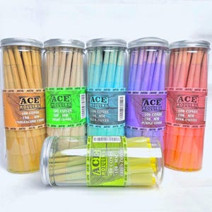 Pode incluir: Seis recipientes cilíndricos de plástico transparente cheios de cones pré-enrolados Ace Rolling. Cinco frascos altos contêm 100 cones cada nas cores cru, cânhamo, azul, roxo e rosa. Um frasco mais curto contém 50 cones verdes. Todos medem 108 mm.