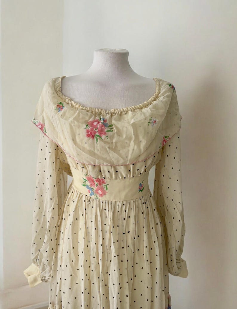May include: A vintage cream-colored dress with a floral print and black polka dots. The dress has a ruffled neckline and long sleeves.