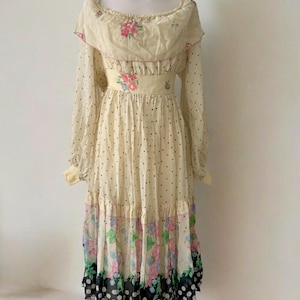 May include: A vintage yellow maxi dress with a floral print and black polka dots. The dress has a ruffled neckline, long sleeves, and a tiered skirt.