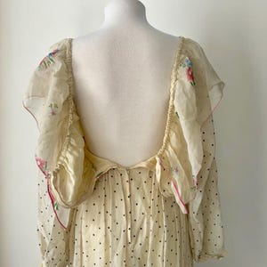 May include: A white maxi dress with a floral print and black polka dots. The dress has a low back and long sleeves with ruffles at the shoulders.