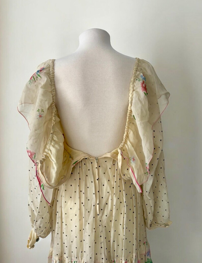May include: A white maxi dress with a floral print and black polka dots. The dress has a low back and long sleeves with ruffles at the shoulders.